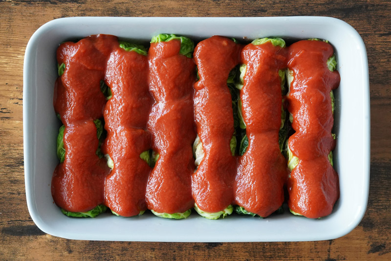 Uncooked cabbage rolls in the pan with sauce on top