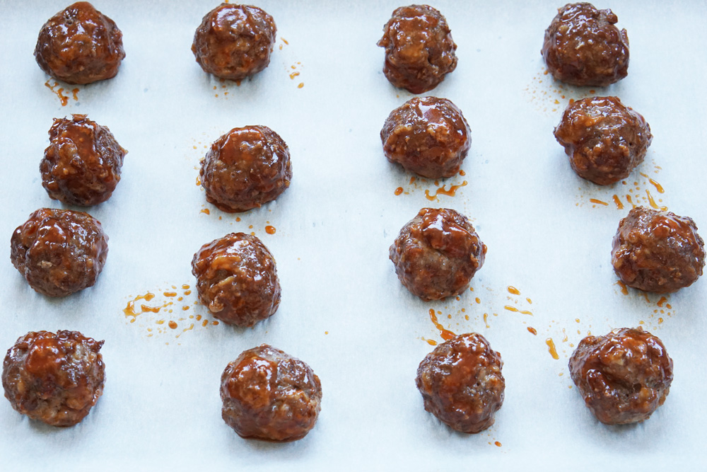 partly cooked meatballs with honey sriracha sauce on a baking sheet
