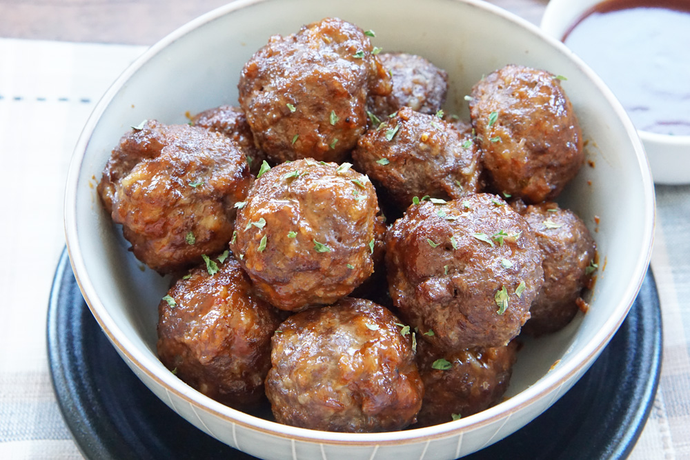 A bowl of honey sriracha meatballs with extra sauce for dipping.