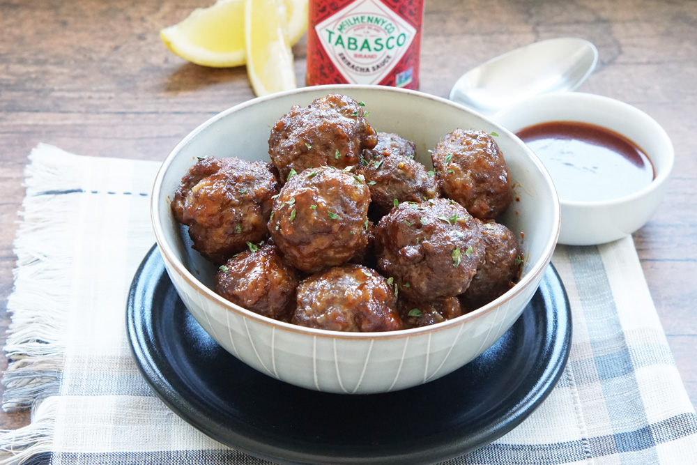 A bowl of honey sriracha meatballs with extra sauce for dipping.